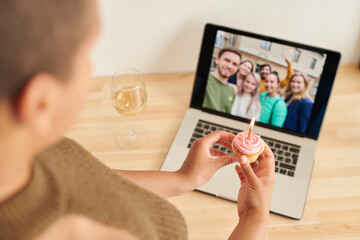 Over shoulder view of black woman holding cupcake with burning candle and celebrating birthday with...