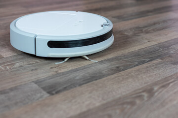 a white vacuum cleaner robot on a laminated wooden floor. The concept of cleaning the living space