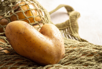 Heart shaped ugly potato on green string bag