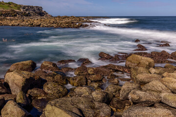 Peaceful long exposure view of breaking waves washing on the rocks at Clovelly Beach, Randwick, Sydney, Australia, with the blurry images of swimmers enjoying the water. 