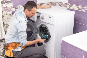 working man plumber repairs a washing machine in laundry