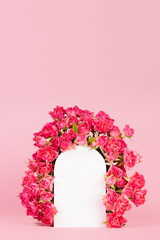 Spring pink flowers - roses as framing of white arch on abstract pink stage mockup for showing of cosmetic products, goods, advertising, design, vertical, copy space. Fresh floral romantic background.