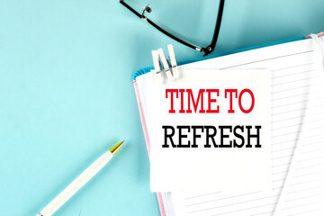 TIME TO REFRESH text on a sticky on notebook with pen and glasses , blue background