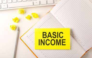 BASIC INCOME text on sticker on the diary with keyboard and pencil