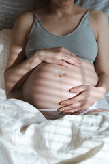 Fototapeta na wymiar A pregnant woman strokes her belly with a baby before childbirth while relaxing in a sunny bright bedroom lying on a bed. Women's health, pregnancy, conception, childbirth concept.