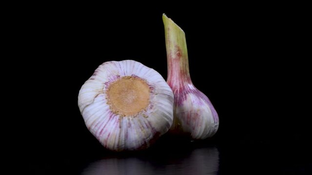 Two heads of young garlic rotate on a black background, close-up.