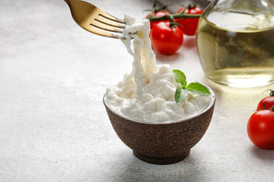 Stracciatella cheese on grey background with fork, oil, basil and tomatoes. Curd cheese product.