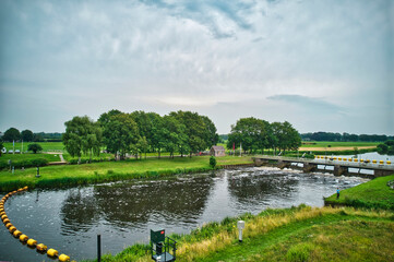 Fototapeta na wymiar Drone view of the river Vecht, green grass, trees, beautiful blue sky and cycle path through the Vecht valley. Bridge and weir in the river. Dalfsen Netherlands