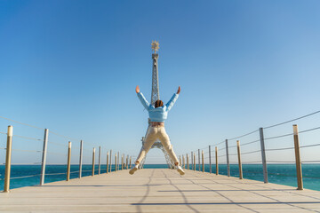 Large model of the Eiffel Tower on the beach. A woman walks along the pier towards the tower,...