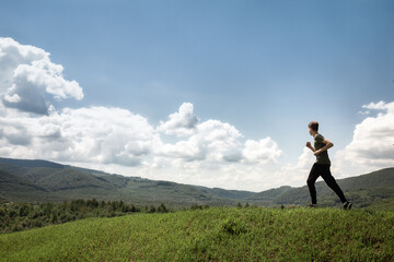 Fototapeta na wymiar Light-skinned male runner running from grass top of mountain hill. Healthy man jogging 