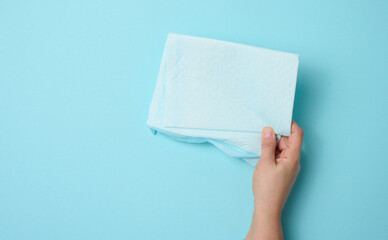 female hand holds a disposable medical diaper on a blue background. Hygiene product
