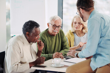 A young educator in classroom showing to senior students lesson on tablet.