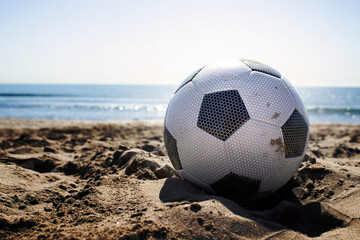 beach landscape with a soccer ball on the sand under a summer sun and in the background the water and the blue sky