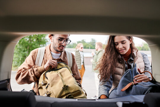 Young multi-ethnic friends loading bags into car trunk while preparing for travel