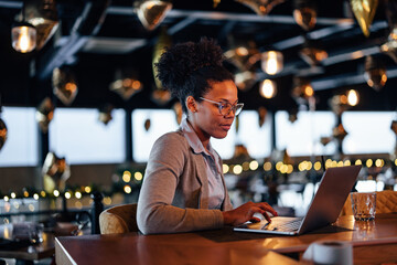 Lovely african-american female novelist, writing her book on her laptop, at a cafe.
