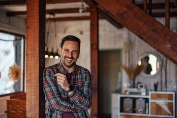 A portrait of a smiling man leaned on the wooden pole, standing and posing indoors.