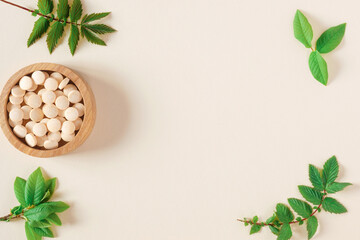 Directly Above Shot Of Pills and green leaves. Tablets in wooden bowl on beige neutral colors background. Homeopathic medicine. Organic medical capsules with herbal plant. Table top view. Copy space - obrazy, fototapety, plakaty