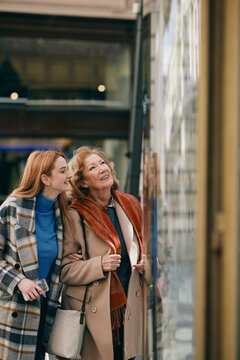 Grandmother and adolescent granddaughter are having fun while shopping and looking through the shop window.