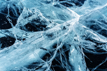 Transparent dark blue ice of frozen Baikal lake with white cracks pattern. Beautiful winter nature background.