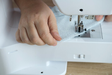 close-up of female hands perform work on a white sewing electric computer machine, stitches appear step by step on the fabric, concept of tailoring, women's hobby, modern needlework