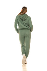 Rear view of a young woman in a green tracksuit posing to a white background in the studio.