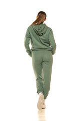 Fototapeta premium Rear view of a young woman in a green tracksuit posing to a white background in the studio.
