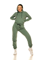 Front view of a young happy woman in a green tracksuit and hood posing to a white background in the studio