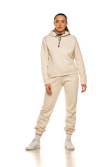 Front view of a young woman in a beige tracksuit posing to a white background in the studio