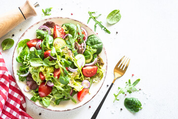 Green salad on white background. Fresh salad leaves and vegetables in white plate. Top view image.
