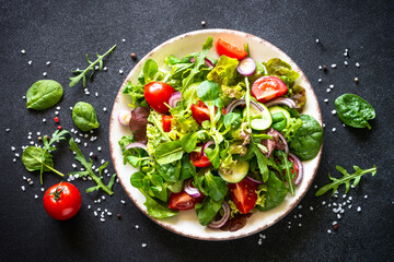 Green salad. Fresh salad leaves and vegetables in white plate at black table. Top view image with copy space.