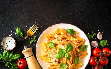 Pasta with tomato sauce, basil and parmesan with ingredients for cooking on dark table. Top view with copy space.