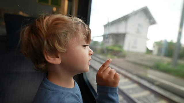 Child travels by train leaning on window pointing at landscape passing by