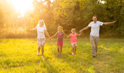 Naklejka na ściany i meble Happy family walking in field and looking at sunset