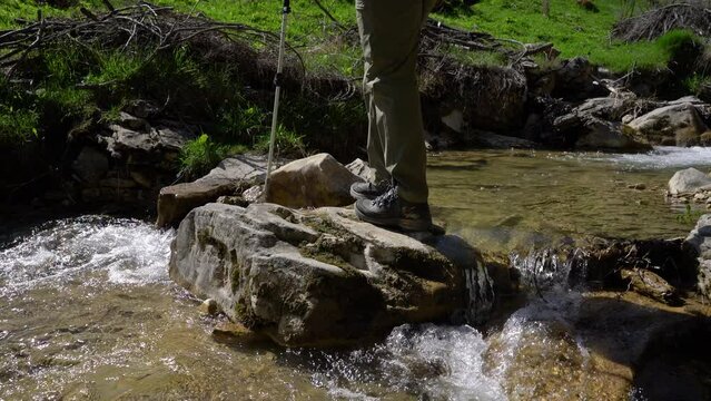 Mountaineer crosses the river from stone to stone - (4K)