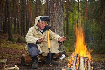 Virtual reality glasses on the head of a guy who warms his hands by a campfire in the woods.