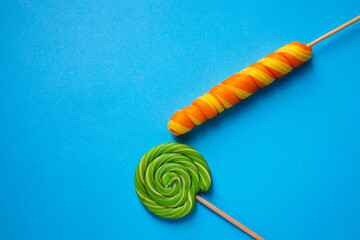 Two multi-colored lollipops of different shapes on a blue background. Space copy.