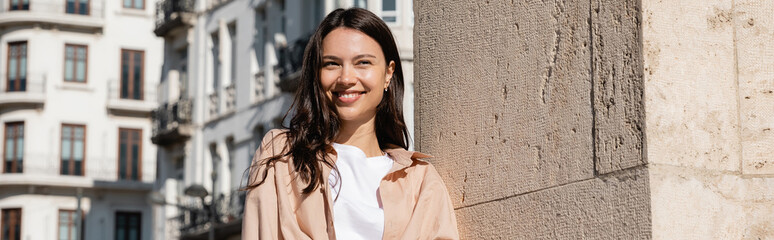 happy brunette woman smiling on city street near wall, banner.