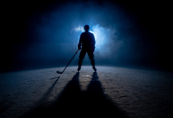 Dark silhouette of a male hockey player in a uniform, helmet and skates with a stick on the ice...