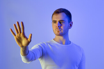 Naklejka premium Contemporary young man posing in various poses in studio.Futuristic neon lighting.Touching screen.