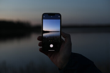 hand holding smart phone and taking photo of beautiful sunset