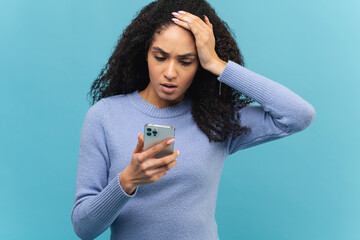 Shocked curly brunette young woman holding smartphone, looking at mobile phone screen and has...