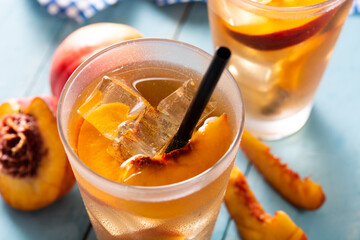 Glass of peach tea with ice cubes on blue wooden table