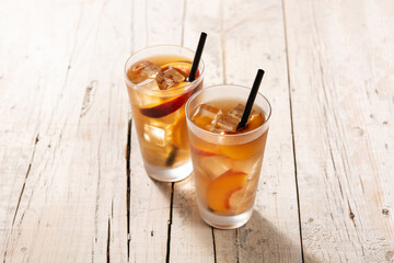 Glass of peach tea with ice cubes on wooden table