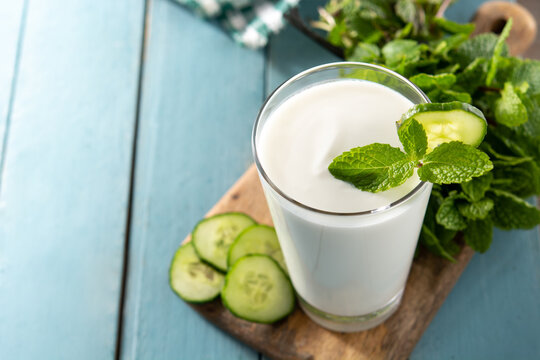 Ayran drink with mint and cucumber in glass on blue wooden table. Copy space