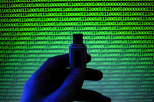 USB flash drive on a background of green binary code. Image of binary code, green numbers on a black background. A man holds a USB flash drive on the background of a computer monitor