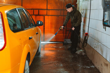 Washing a yellow car at a contactless self-service car wash. Washing a sedan car with foam and high-pressure water.