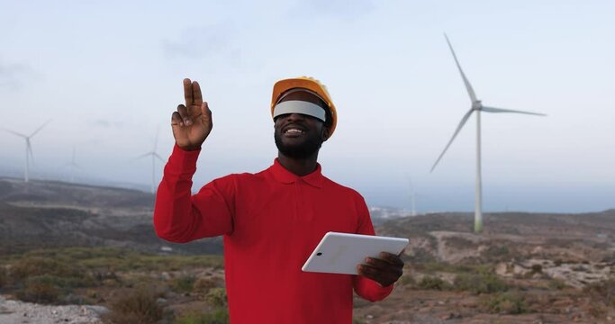 African engineer working at windmill farm using digital tablet and virtual realtiy goggles 