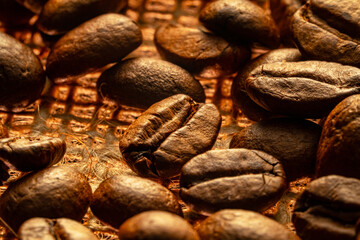 Dark brown roasted coffee beans lying on burlap. Organic coffee seeds close up. Food and drink background for cafe and cafeteria. Grains for the preparation of an invigorating and strong morning drink