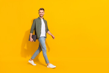 Fototapeta na wymiar Full length body size view of attractive cheerful guy holding laptop going copy space isolated over bright yellow color background