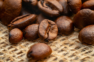 Dark brown roasted coffee beans lying on burlap. Organic coffee seeds close up. Food and drink background for cafe and cafeteria. Grains for the preparation of an invigorating and strong morning drink